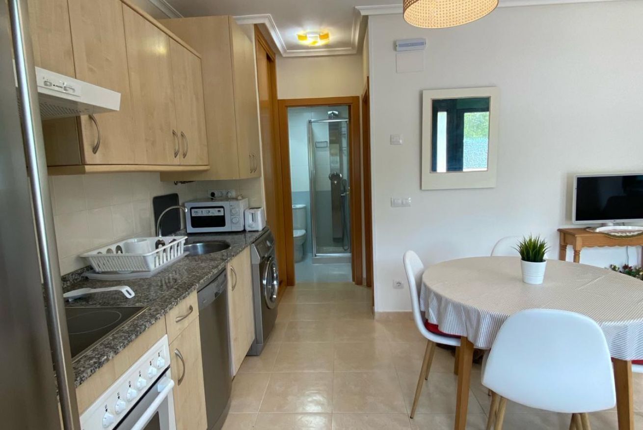 A modern kitchen with granite countertops, a built-in oven, and a microwave. There is a dining area with a round table and chairs, and a small potted plant on the table.