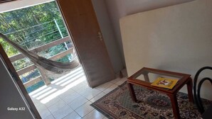 Ein Balkon mit einer Hängematte, einem kleinen Tisch mit einem Buch und einem gemusterten Teppich.