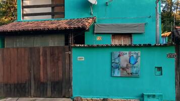 Um edifício de dois andares com fachada verde, uma antena parabólica e uma placa com a inscrição 'CASA POUSA'.