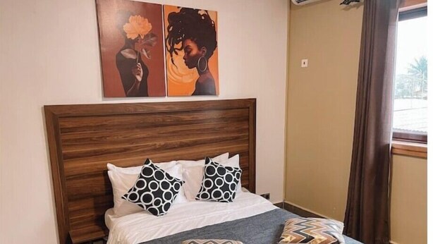 A bed with a wooden headboard, two patterned pillows, a grey throw blanket, and two wall art pieces depicting floral and abstract designs.