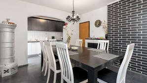 A modern kitchen with white cabinets, a black brick accent wall, and a dining area with white chairs and a dark wooden table. - Pet friendly apartment in Rab with WiFi (Rab)