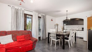 A modern living room with a red sofa, dining area with white chairs, and a kitchen with dark cabinets. - Pet friendly apartment in Rab with WiFi (Rab)