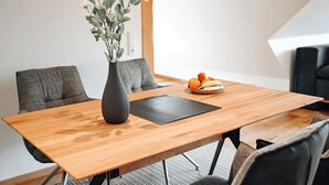 A modern dining area with a wooden table, grey upholstered chairs, a black placemat, and a vase with white flowers. - LakeviewOasis: Exclusive Schnepfhalde apartment (Schluchsee)