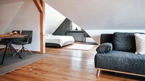 A modern loft bedroom with a sloped ceiling, a bed, a desk with a chair, and a gray sofa. - LakeviewOasis: Exclusive Schnepfhalde apartment (Schluchsee)