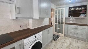 Cocina compacta con lavadora, armarios grises y encimera de madera.