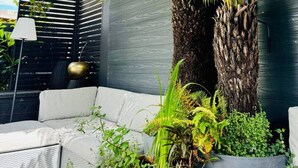 A modern outdoor seating area with a sofa, a potted fern, and a tall palm tree. - Luxury! Modern `Chic` home off Central Mill Road (Cambridge)