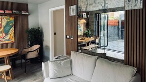 A modern living room with a sofa, a dining table with chairs, a large abstract painting, and a view through a glass door. - Luxury! Modern `Chic` home off Central Mill Road (Cambridge)