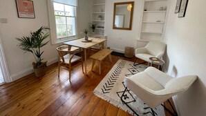 A living room with a wooden floor, a dining table with chairs, a white armchair, a patterned rug, a hanging light fixture, and a bookshelf. - Amazing Victorian House, Excellent City Location (Cambridge)
