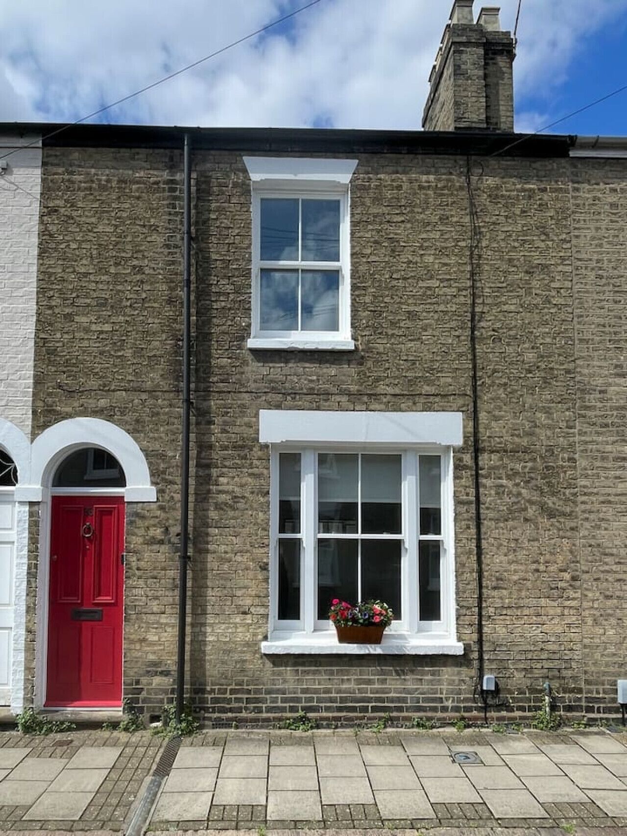 Un edificio de ladrillo de dos pisos con una puerta roja y una ventana con un macetero.