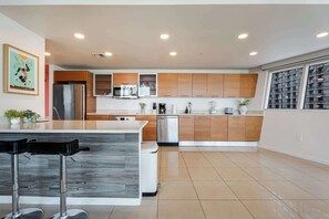 A modern kitchen with a central island, stainless steel appliances, wooden cabinets, and a large window.