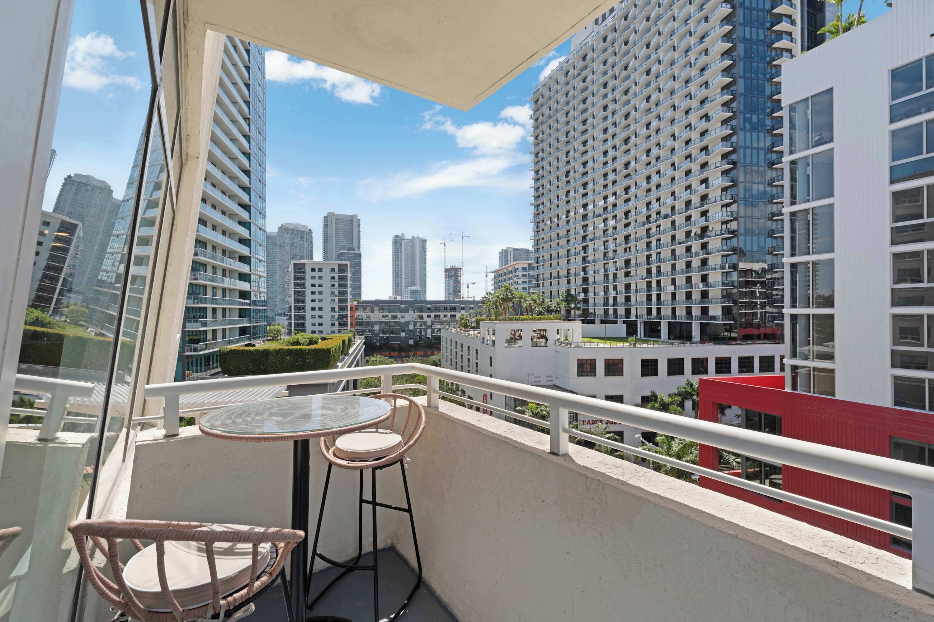 Ein Balkon mit Glastisch und Korbstühlen, mit Blick auf eine Stadtlandschaft mit Hochhäusern.