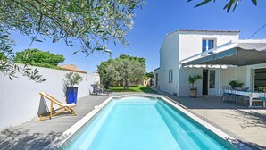 Piscina com deck de madeira e espreguiçadeiras, cercada por um edifício branco com varanda coberta.