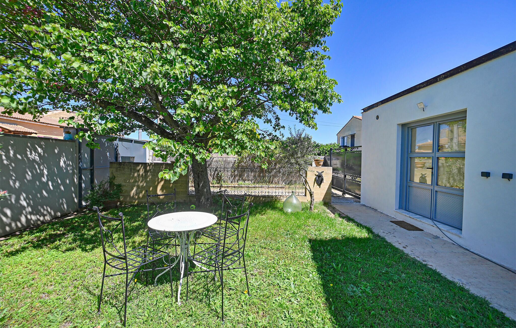 A backyard with a metal table and chairs, a tree, and a house with a blue door.