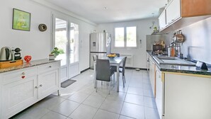Uma cozinha moderna com armários brancos, uma mesa de jantar com cadeiras, uma geladeira e uma pia.