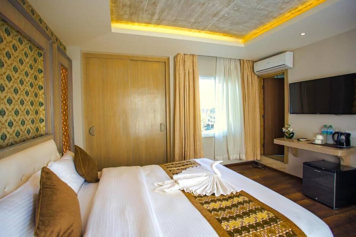 Een hotelkamer met een groot bed, een bureau met een flatscreen televisie, een airconditioning en een raam met gordijnen.