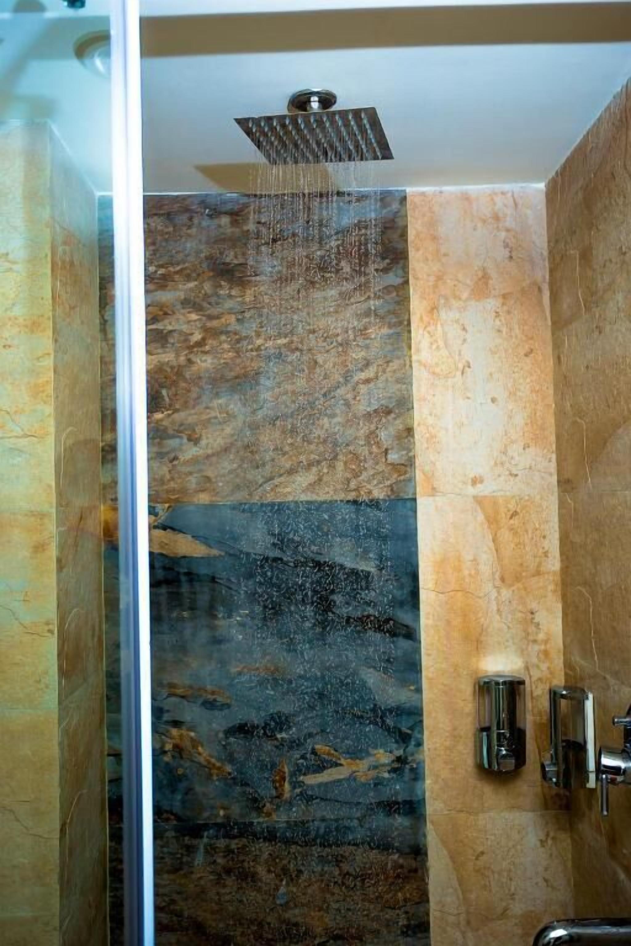 A shower with a rain-like water feature, a glass partition, and a wall with a marble-like texture.