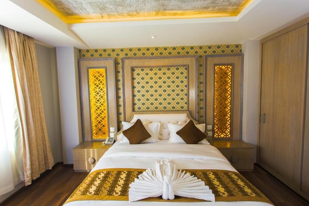 A hotel room with a large bed, two nightstands, a wooden wardrobe, and decorative panels on the walls.