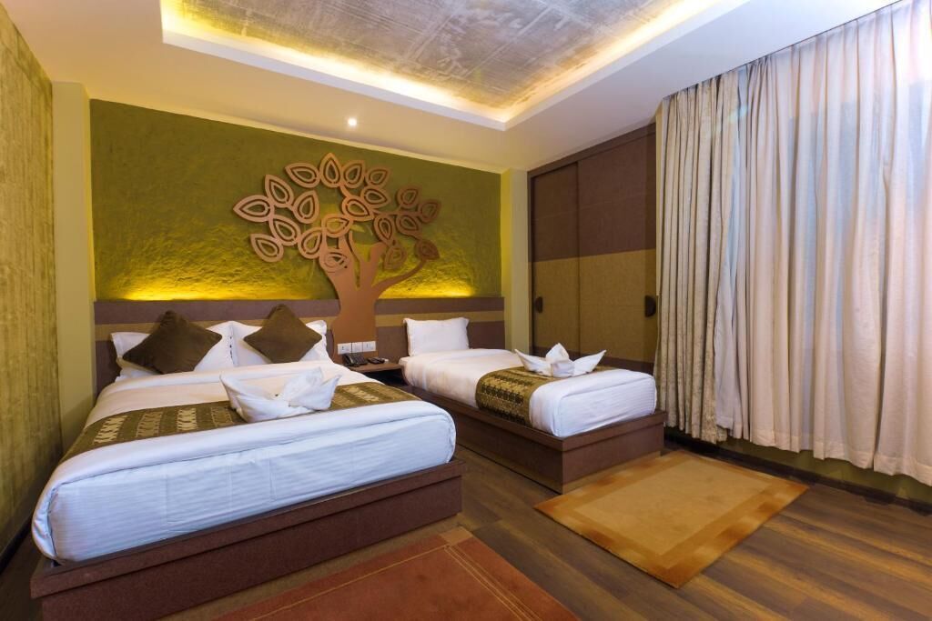 A hotel room with two beds, a decorative tree wall art, a large window with curtains, and a wooden floor.