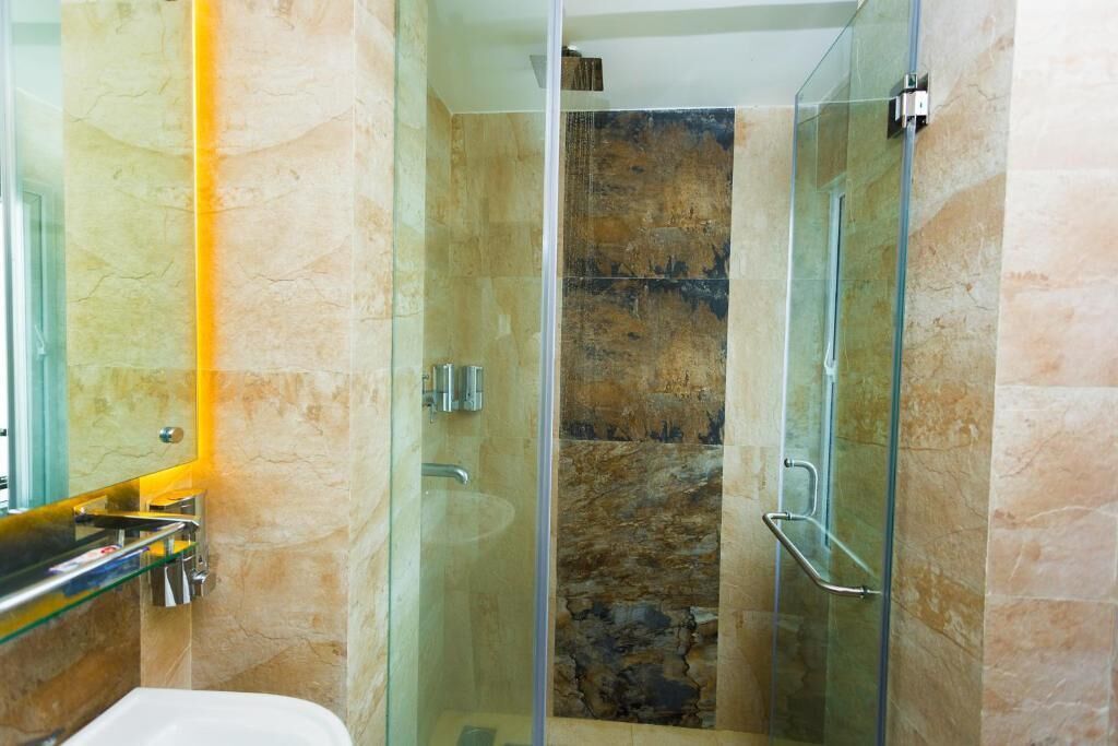 A modern bathroom with a glass-enclosed shower, marble walls, and a glass sink.