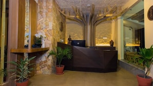 Un área de recepción con pared de piedra, un mostrador de madera y plantas en macetas.