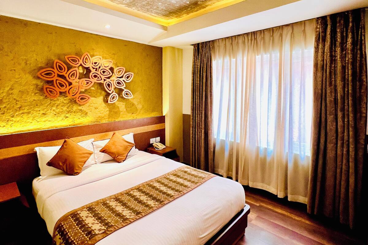 Hotelkamer met een groot bed, een decoratief wandkunstwerk, een houten hoofdbord, een nachtkastje met een lamp en een raam met gordijnen.