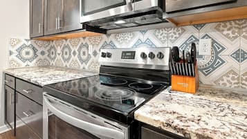 A kitchen with a stainless steel stove, oven, and microwave. There is a patterned backsplash and a knife block on the countertop.