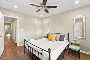 Une chambre à coucher comprenant un lit, une table de chevet, un miroir, un ventilateur de plafond et un couloir.
