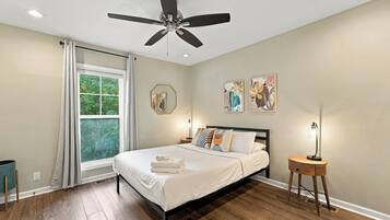 A bedroom with a bed, a ceiling fan, a window with curtains, and artwork on the wall.