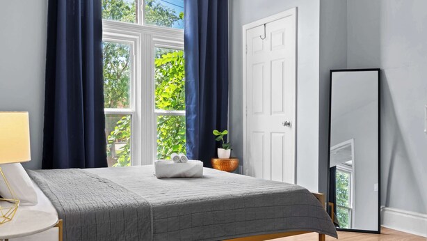 A bedroom with a bed, a bedside table, a mirror, and a window with curtains. - 3BR Relaxing Home in Louisville's Prime Location! (Louisville)