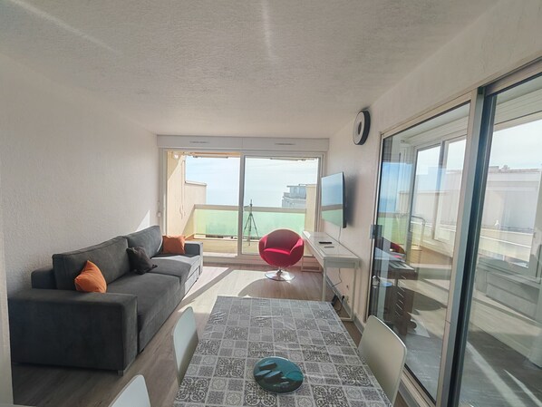 A modern living room with a sofa, a dining table, a red chair, and a TV.