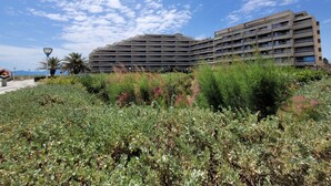 A modern multi-story building with a flat roof and horizontal lines, surrounded by dense greenery and a clear sky. - Canet Sud - T2 Cabin 4/6 pers - Terrace - Direct Beach Access (Canet-en-Roussillon)