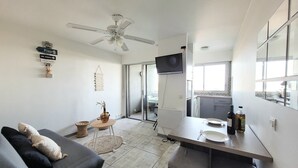 Un espacio habitable compacto con sofá, una mesa de comedor con televisor, kitchenette y ventilador de techo.