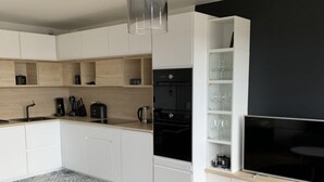 Een moderne keuken met witte kastjes, een zwarte koelkast en een grote flatscreen televisie aan de muur.