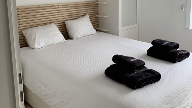 Een slaapkamer met een bed, witte beddengoed, een houten hoofdbord, een hanglamp en een spiegel.