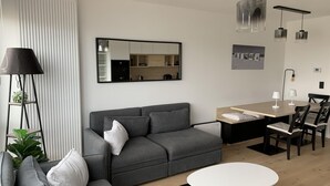 Een moderne woonkamer met een grijze bank, een eettafel met stoelen, een kleine ronde tafel en een vloerlamp.