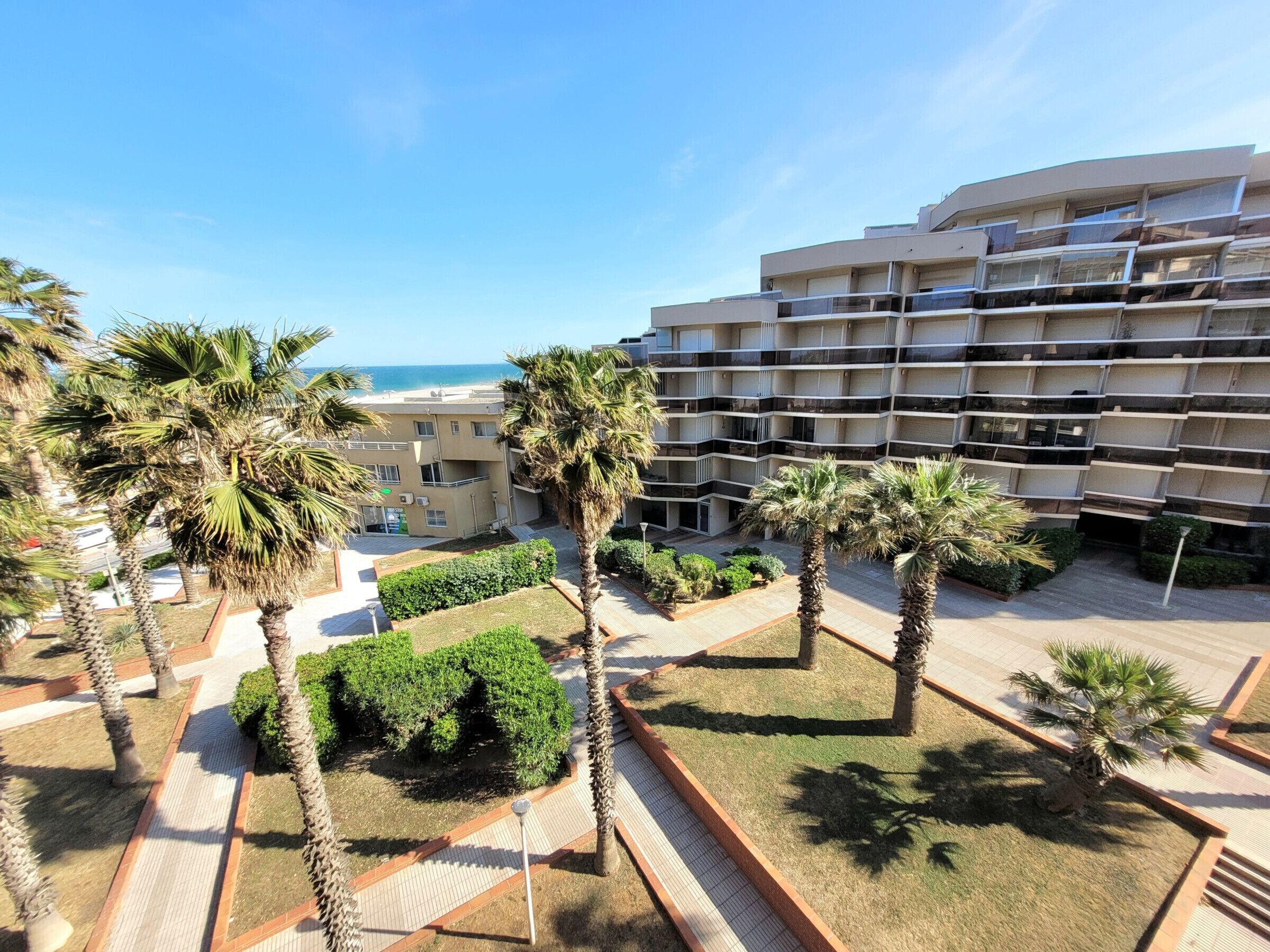 Un hôtel moderne doté de nombreux balcons, de palmiers et offrant une vue sur la plage.