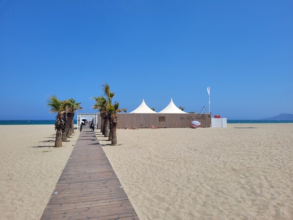 A beach with a wooden walkway leading to a white tented structure labeled "LA NNL VAGUE".