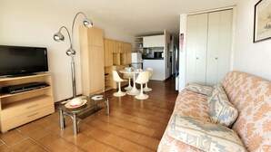 Una sala de estar con televisión, una mesa de centro de vidrio, sofá y un comedor con sillas y mesa.