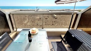 A balcony with a view of the beach, a table with a bottle of wine, a hat, and a striped umbrella. - Canet-en-Roussillon - Studio 2 pers - Sea view - Quiet residence (Canet-en-Roussillon)