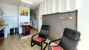 A compact living space with a kitchenette, two chairs, a dining table, and a large window with curtains. - Canet-en-Roussillon - Studio 2 pers - Sea view - Quiet residence (Canet-en-Roussillon)
