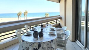 A round table with a tablecloth, white chairs, and a bottle of wine on a balcony overlooking a beach. - Canet - T2 cabin, 5 pers, beach access, pool, parking (Canet-en-Roussillon)
