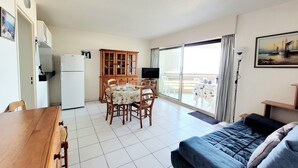 A compact living space with a dining area, a sofa, a TV, and a balcony with a view. - Canet - T2 cabin, 5 pers, beach access, pool, parking (Canet-en-Roussillon)