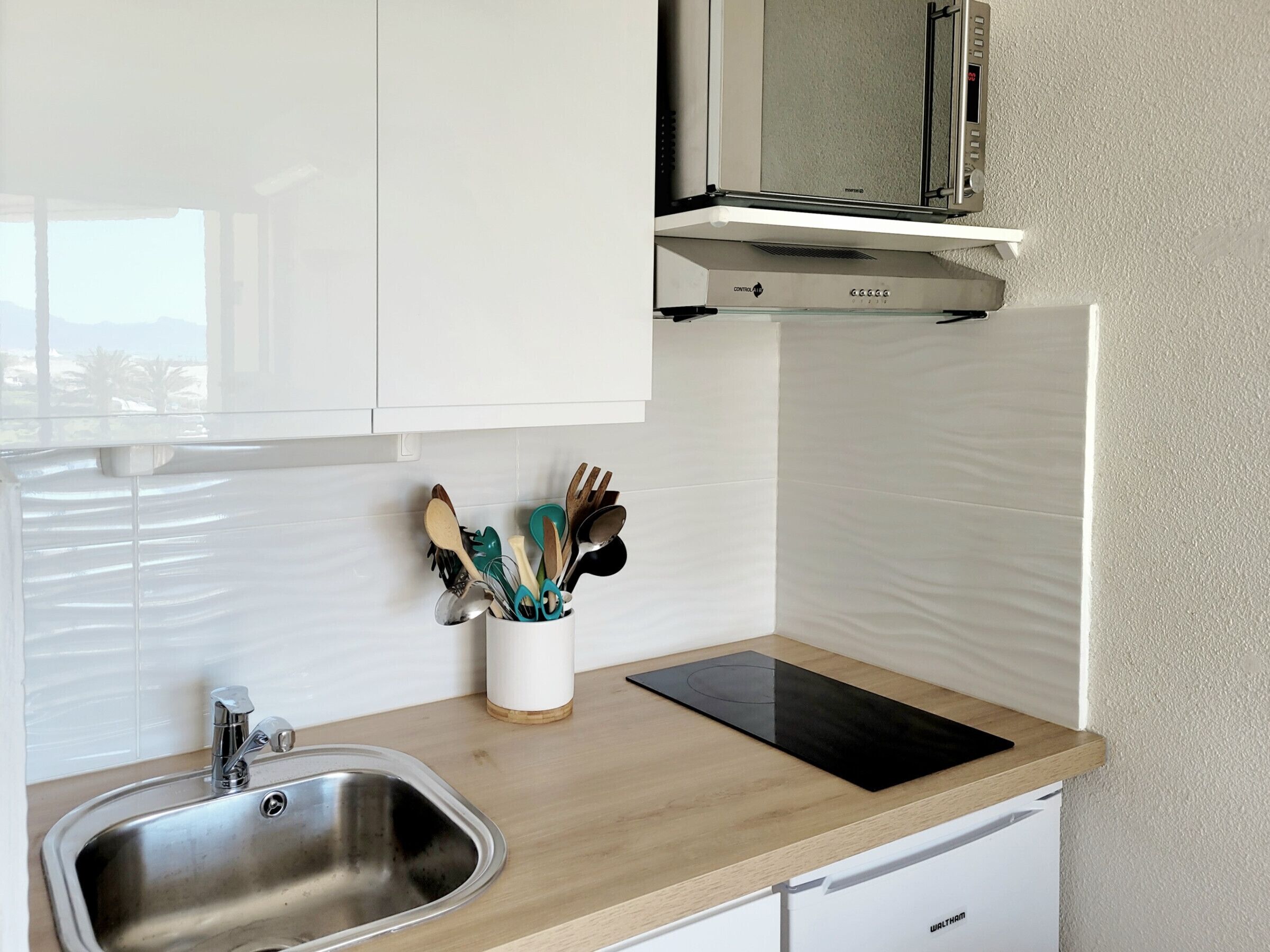 A modern kitchen with a stainless steel sink, wooden countertop, and a built-in microwave.