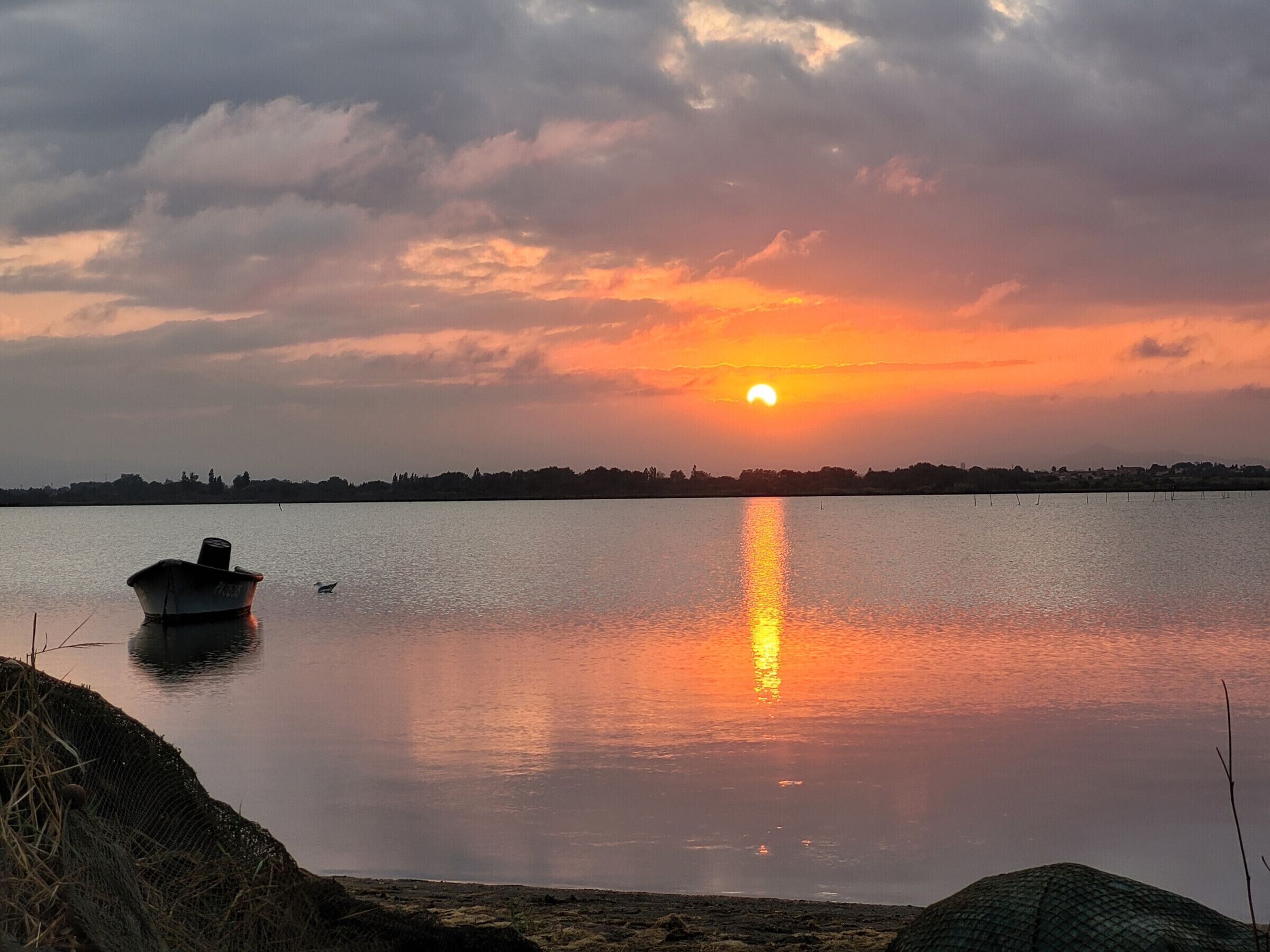 A calm lake at sunset with a boat and a distant shoreline.
