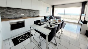 A modern kitchen with a dining area, a large window with a view of the sea, and a balcony. - Canet-en-Roussillon - 6 ppl - T3 - Beach Access, Parking, Pool, Wifi (Canet-en-Roussillon)