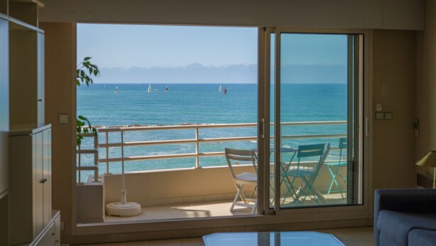 Een balkon met uitzicht op zee, een tafel en stoelen.