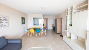 Een moderne woonkamer met een bank, een glazen salontafel, een eethoek met tafel en stoelen, en een kledingkast met planken.