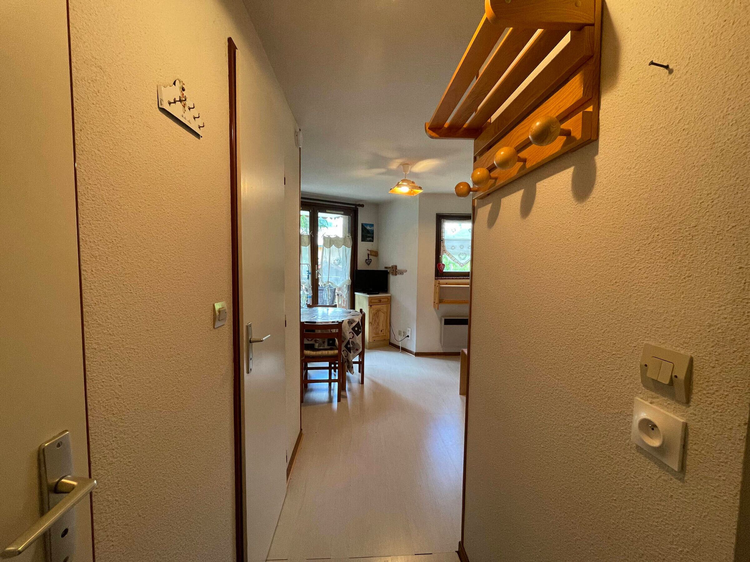 A hallway leading to a dining area with a table and chairs, a kitchen with a window, and a door with a lock.