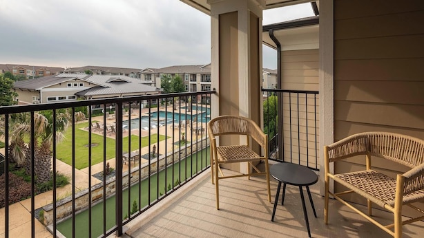 Een balkon met rieten stoelen, uitzicht op een zwembad en een gebouw op de achtergrond.