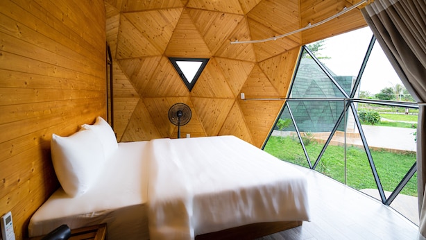 A wooden-paneled room with a bed, a fan, and a window with a view of greenery. - VinaEcolife Lodge (Tan Xuan)
